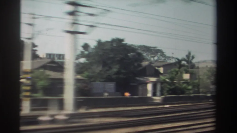 1982 Taiwan train-window view with parallel tracks, overhead lines, utility poles, trees, and low homes blurred by motion.