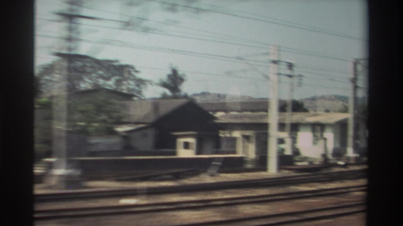 Blurred trackside buildings, poles, wires, and rails seen from a moving train.