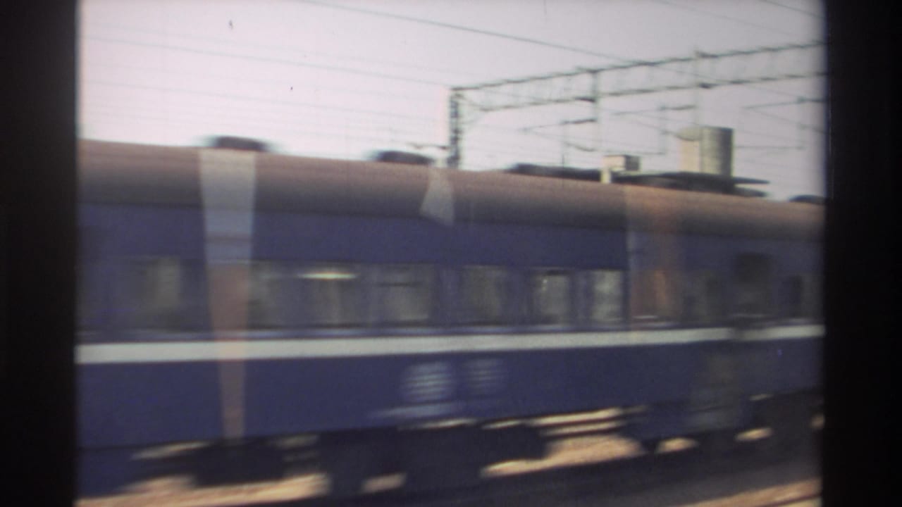 Blue passenger train with a white stripe passing under overhead rail wires.