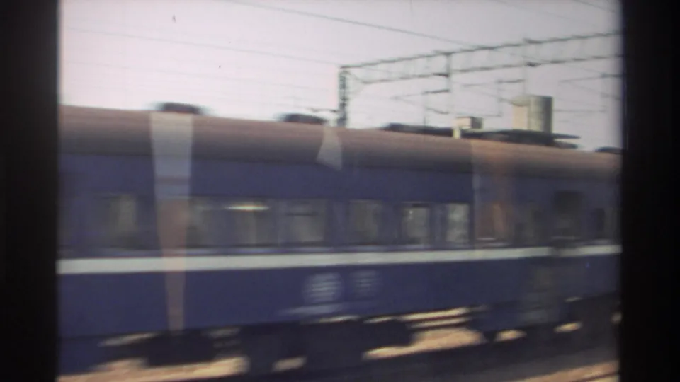 A blue passenger train with a white stripe passes in motion blur beneath overhead wires in this 1982 Taiwan railway view.