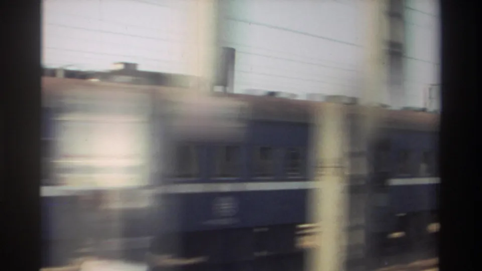 The passing blue train is partly obscured by blurred foreground posts or window edges, emphasizing the moving-train viewpoint in Taiwan, 1982.