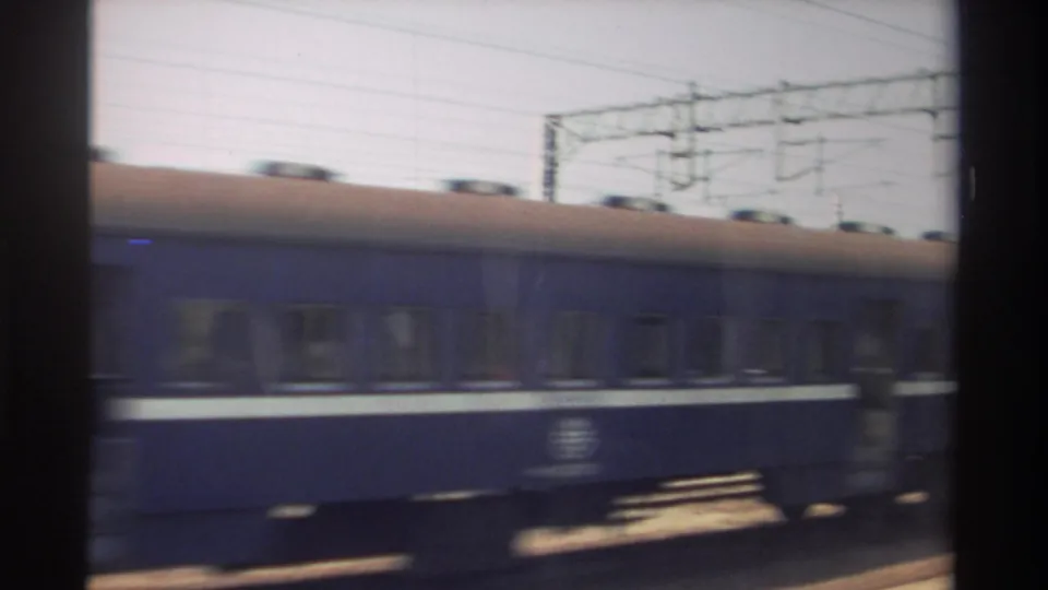 A blue passenger rail car continues past under overhead wiring, with trackside infrastructure visible in the 1982 Taiwan home-movie frame.