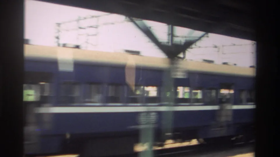 1982 Taiwan 8mm view of a blue passenger train along a station platform, with columns, overhead lines, and indistinct commuters.
