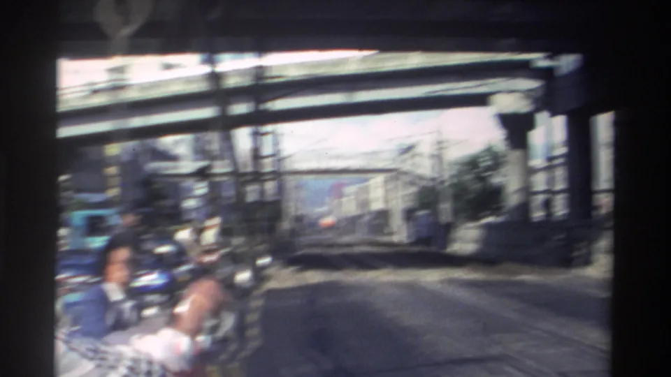 A motion-blurred 1982 Taiwan street view shows scooters, pedestrians, fencing, and elevated rail or roadway structures as the handheld camera swings away.