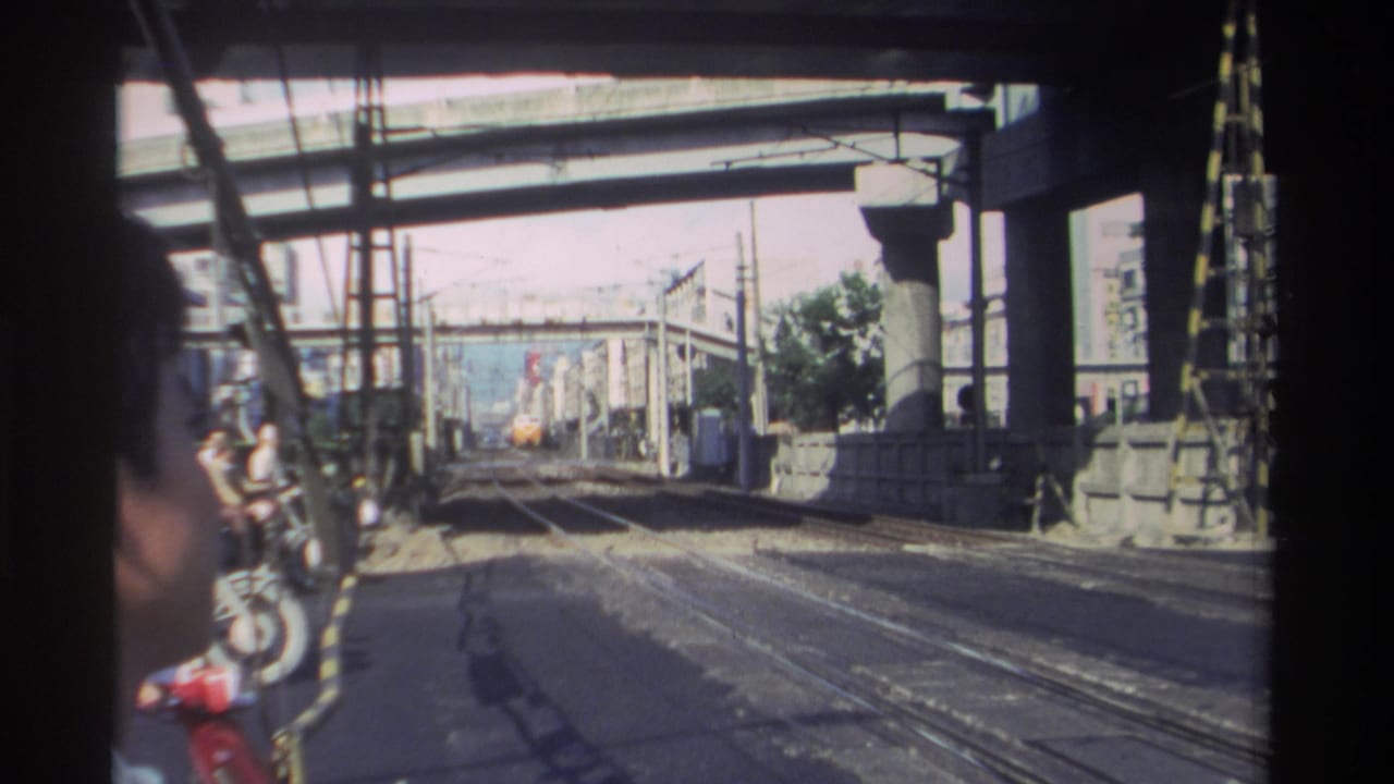 Train tracks under a concrete overpass with a partial face at the left edge.