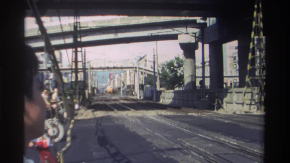 1982 Taiwan 8mm frame showing rail tracks beneath an overpass, with a partial face at left and a train distant ahead.