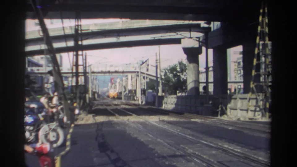 1982 Taiwan 8mm station view showing tracks beneath a concrete overpass, a distant yellow train, and people partly visible at left.