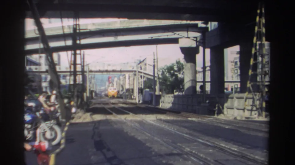 1982 Taiwan home-movie frame of a yellow train aligned with tracks under a concrete overpass, with station structures around it.
