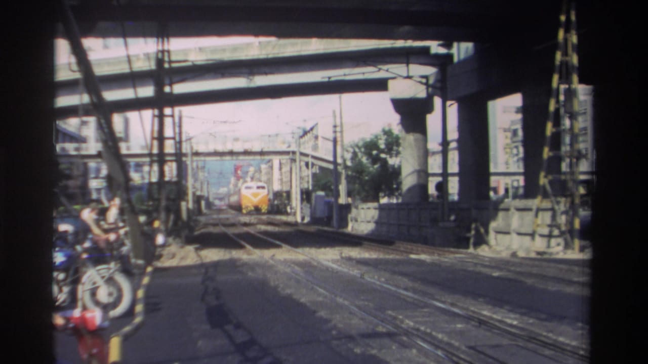 Train continues toward the camera on rails under a large concrete bridge structure.