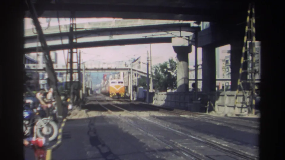 Home-movie view of a train moving closer through an industrial Taiwan rail area beneath elevated concrete infrastructure in 1982.