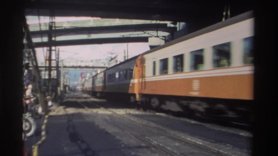 1982 Taiwan rail scene with orange and white passenger cars moving rapidly past a roadside viewpoint under elevated structures.