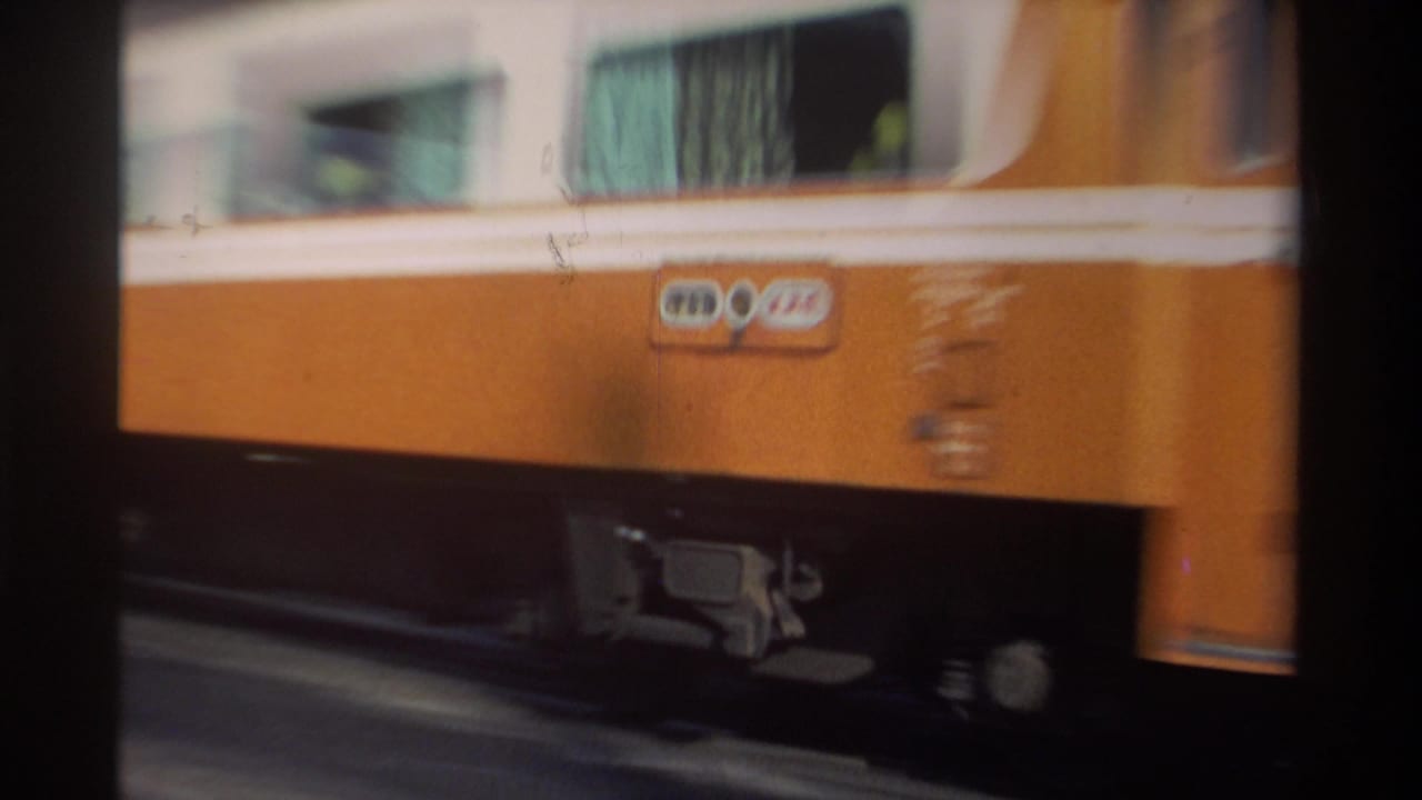 1982 Taiwan home-movie frame showing an orange-and-white passenger train moving past a fixed, partly obstructed viewpoint.