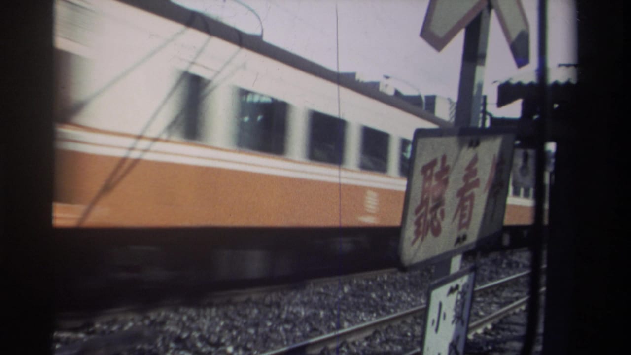 1982 Taiwan frame with a blurred orange-and-white train passing behind trackside warning signs and rail ballast.