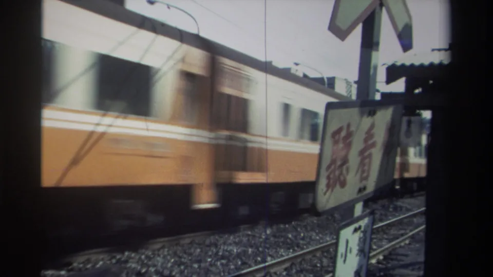 Motion-blurred 1982 Taiwan rail view with an orange-and-white passenger train behind a prominent warning sign near the tracks.