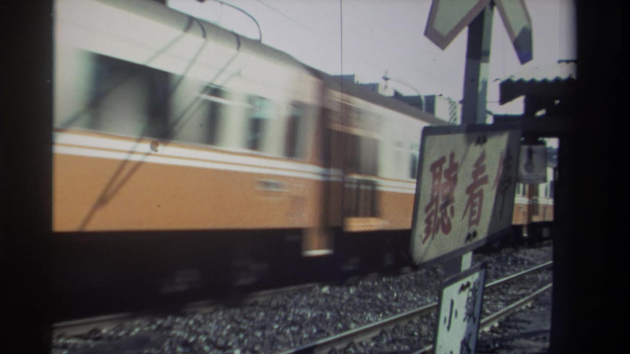 Orange-and-white train passing a railway crossing beside a Chinese-character sign.