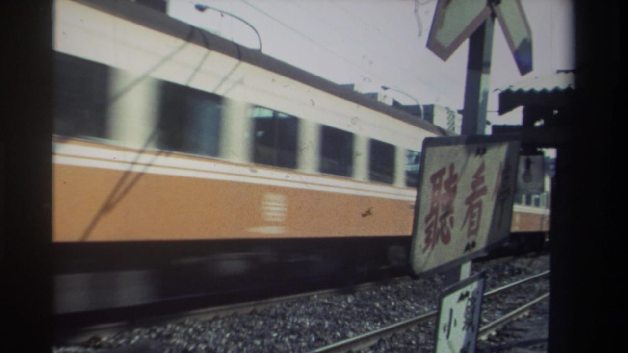 Blurred passenger train moving past rails and a trackside sign.