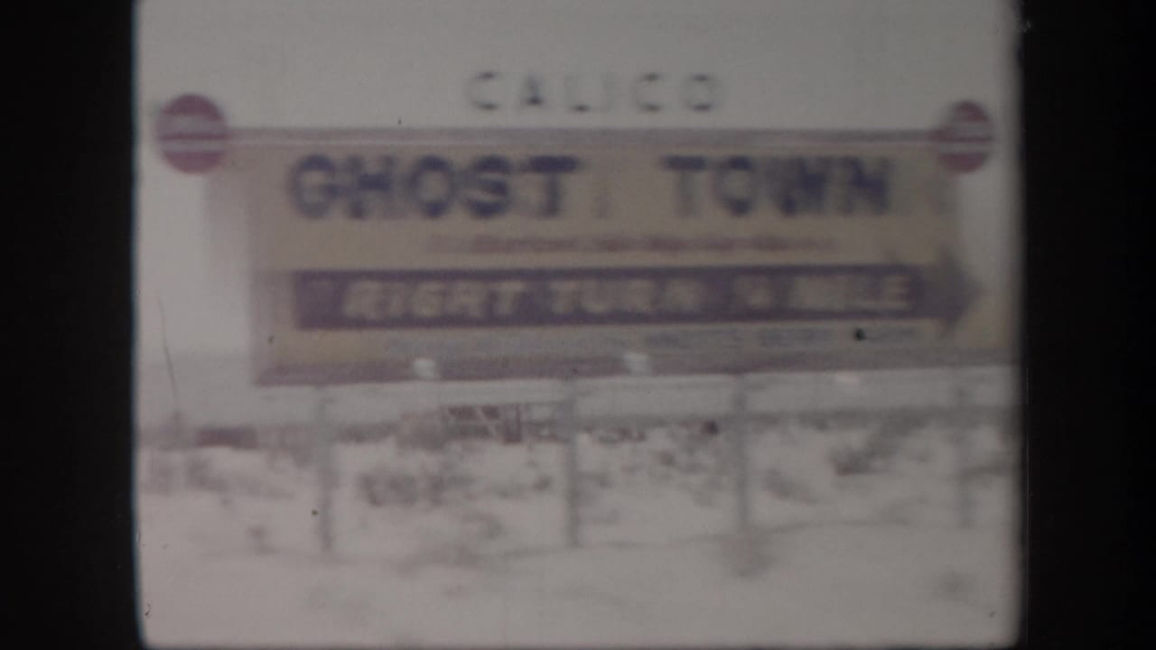 Roadside sign points toward Calico Ghost Town against a pale desert background.