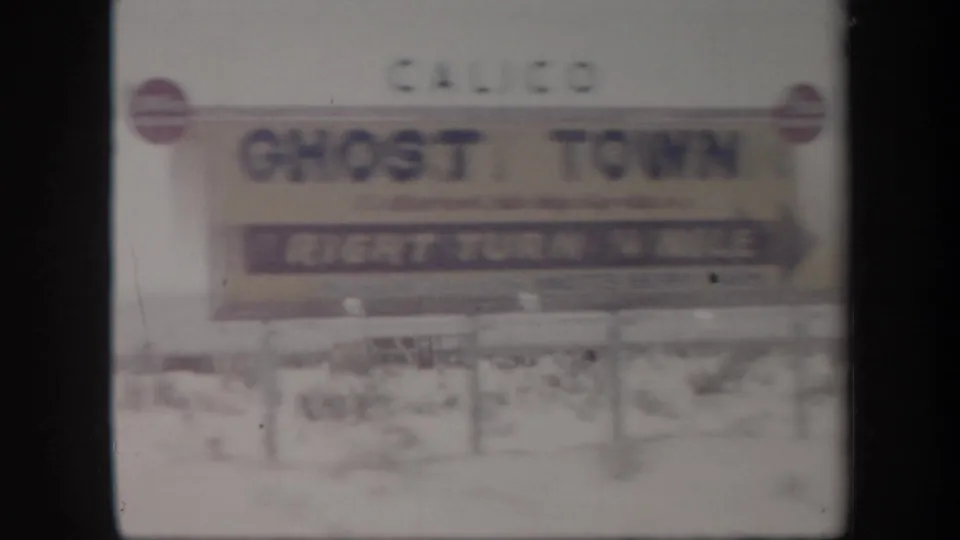 Soft 8mm frame of a Calico Ghost Town roadside sign indicating a right turn, with desert ground behind it.