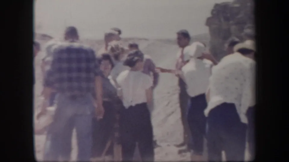 Adults in mid-century clothing stand together in a dusty Arizona outdoor setting, seen in soft 8mm color.