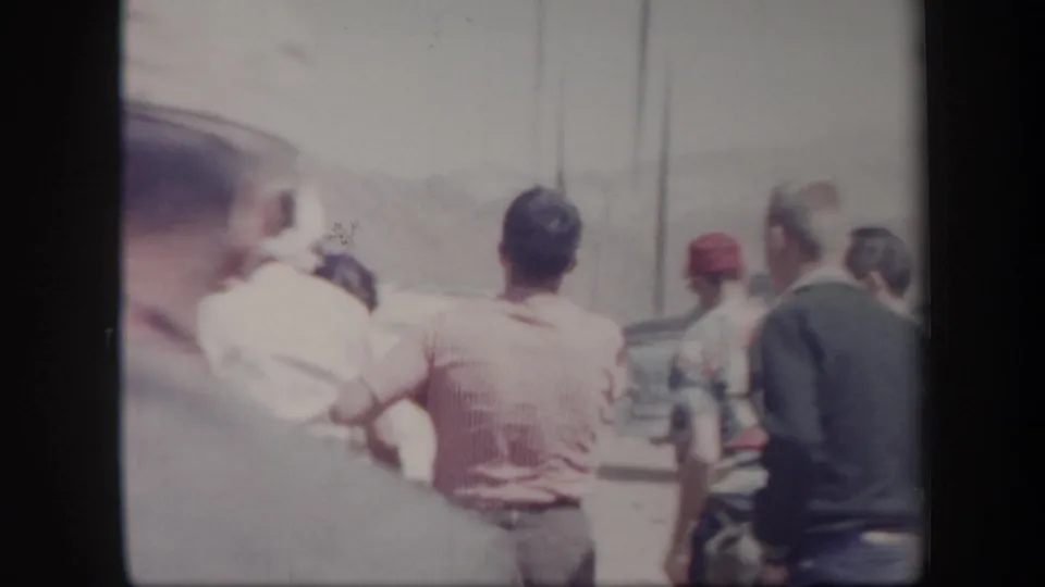 Adults seen from behind near a parked car in a bright 1957 Arizona desert field, captured in faded 8mm color.