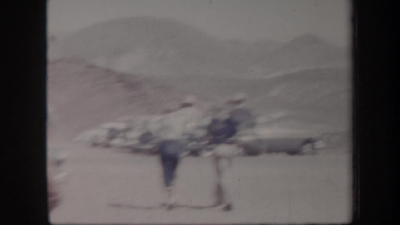 Soft 8mm view of visitors and cars in an Arizona outdoor parking area, with pale hills in the distance.