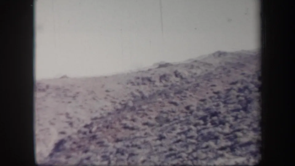 1957 Arizona 8mm frame showing a dry rocky hillside under a pale sky, with soft focus and faded color.