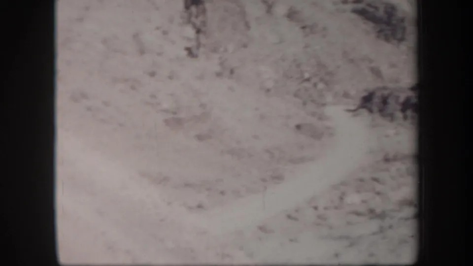 1957 Arizona 8mm frame showing a pale sandy desert slope and rocky hillside, with no person clearly visible in this frame.