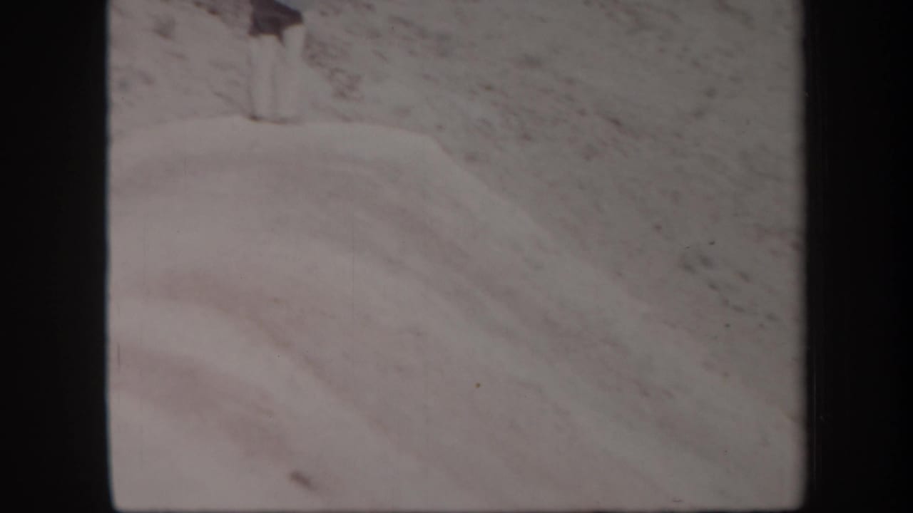 Pale sand dune and rocky desert hillside framed by dark film borders.
