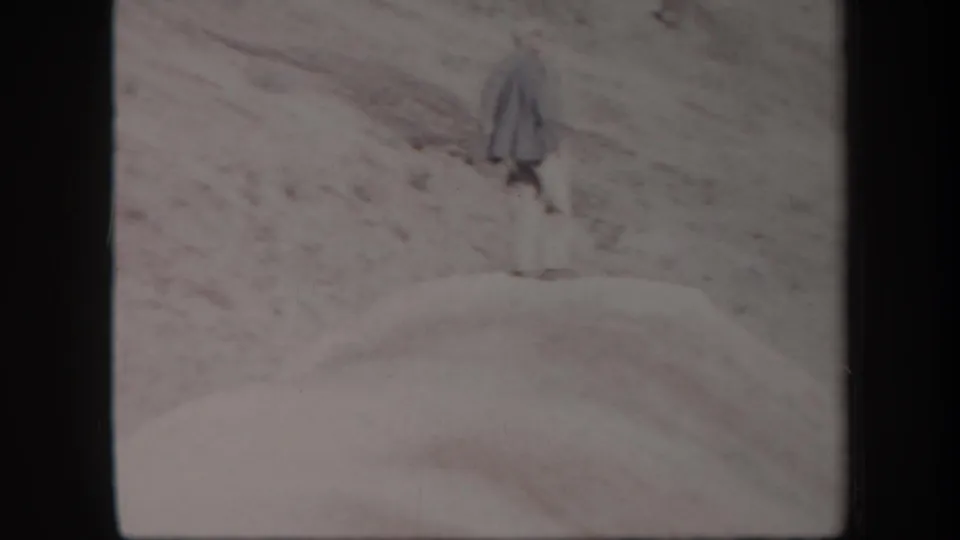 1957 Arizona 8mm frame showing a distant man standing on a sand dune against a barren desert slope.