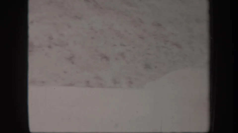 1957 Arizona 8mm frame showing an empty stretch of pale sand and rocky desert hillside after the figure moves out of view.
