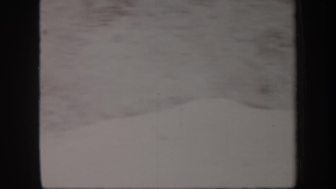 1957 Arizona 8mm frame with a pale rocky hillside, washed dirt road, and dark film gate edges.