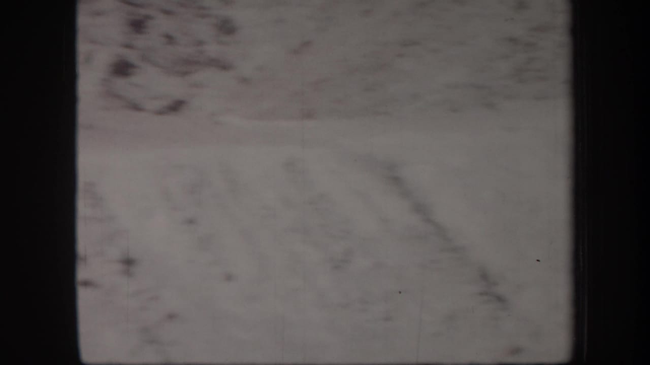 1957 Arizona 8mm frame showing pale mountain terrain, faint sky, dust marks, and heavy gate shadow at the edges.