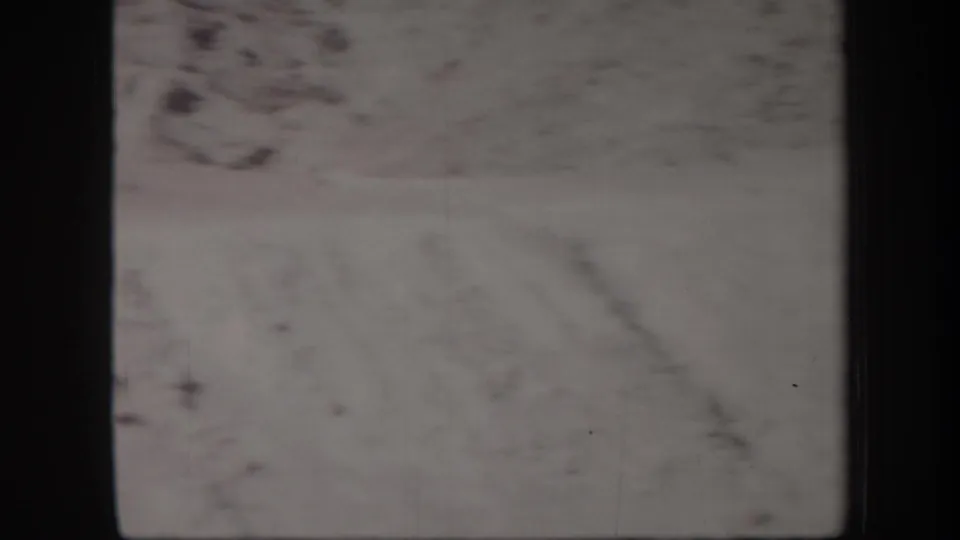 1957 Arizona 8mm frame showing pale mountain terrain, faint sky, dust marks, and heavy gate shadow at the edges.