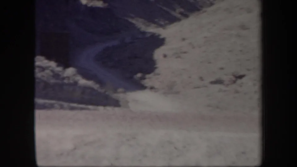 1957 Arizona 8mm frame with a mountain slope, pale dirt or gravel road, rocky ground, and soft color shift.