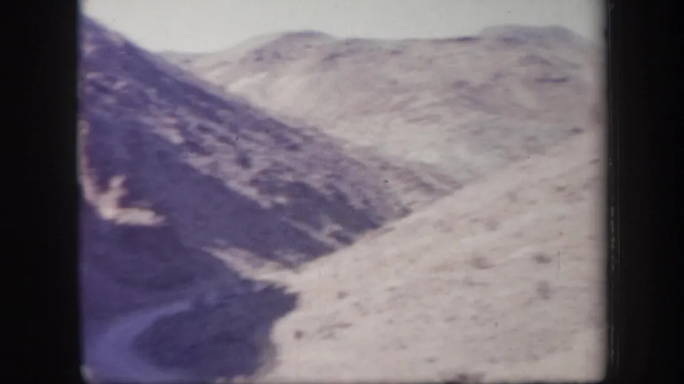 1957 Arizona 8mm frame showing rugged hills, a pale road or wash, bright sky, and handheld home-movie softness.