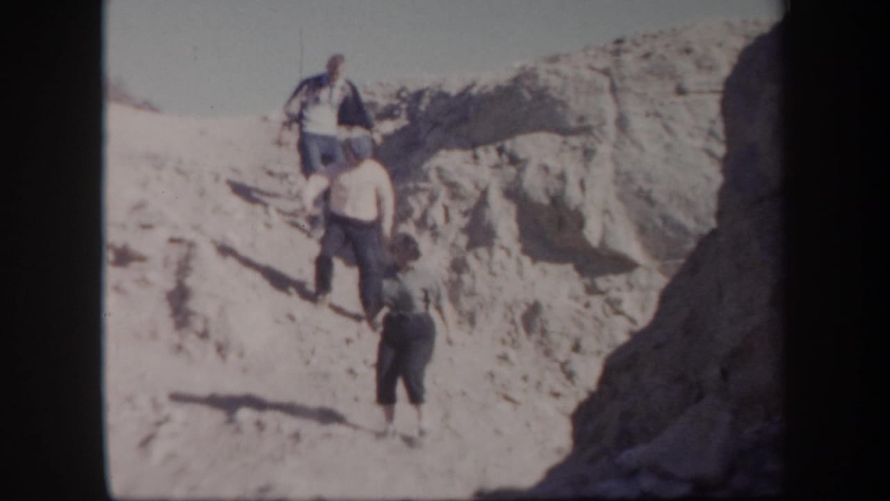 Three adults continue down a sandy incline with eroded desert rock behind them.