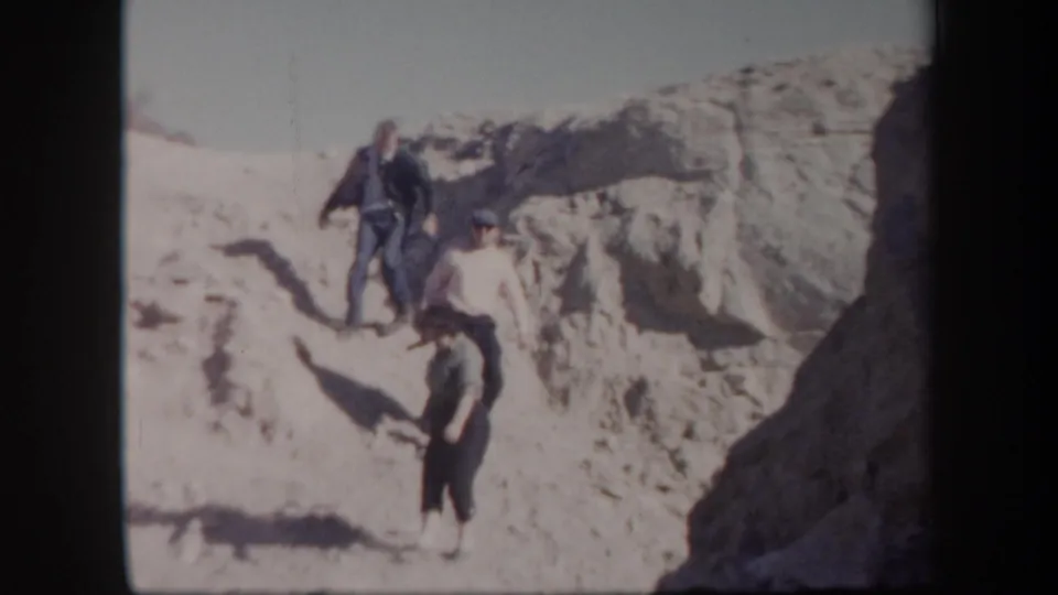 A 1957 Arizona travel frame shows adults descending, with one figure closer to the camera on the sandy terrain.