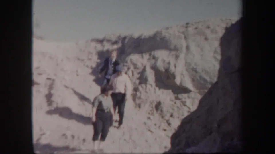 The group reaches a lower part of the Arizona desert slope, framed by pale rock and handheld 8mm exposure.