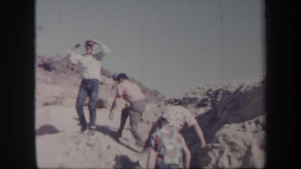 Adult men in casual 1950s clothing appear to hike across rocky Arizona desert terrain in faded 8mm footage.