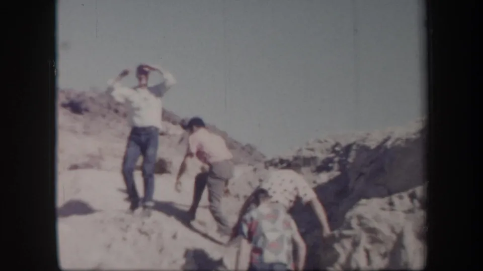 Adult men in casual 1950s clothing appear to hike across rocky Arizona desert terrain in faded 8mm footage.