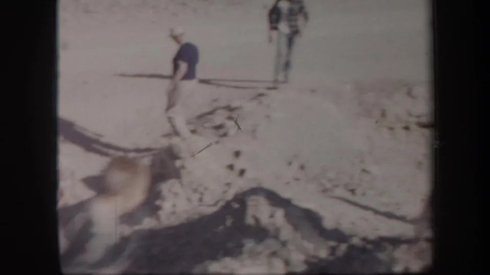 Home-movie frame from the Arizona clip showing a visitor stepping across uneven rocky terrain under strong sunlight.