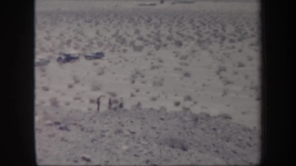1957 Arizona 8mm frame showing small figures in open desert terrain near several parked mid-century cars.