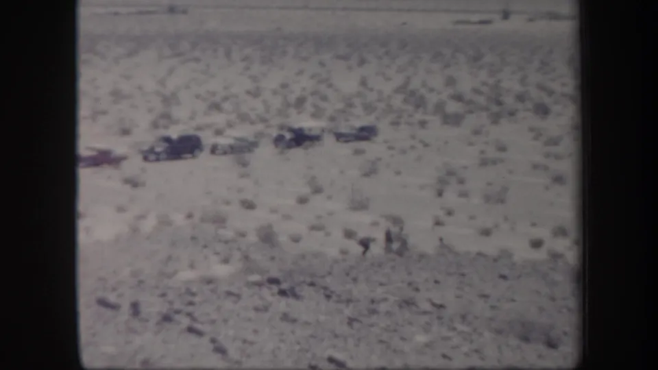 Arizona desert scene from 1957 home-movie footage with parked cars and distant people on sandy terrain.