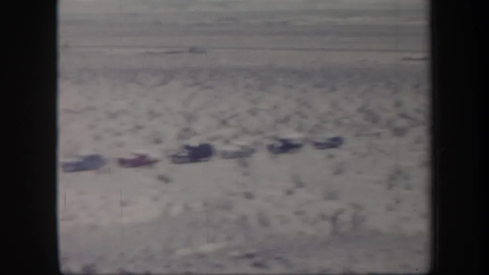 End frame of 1957 Arizona 8mm footage showing a distant line of parked cars in desert scrub with people nearby.