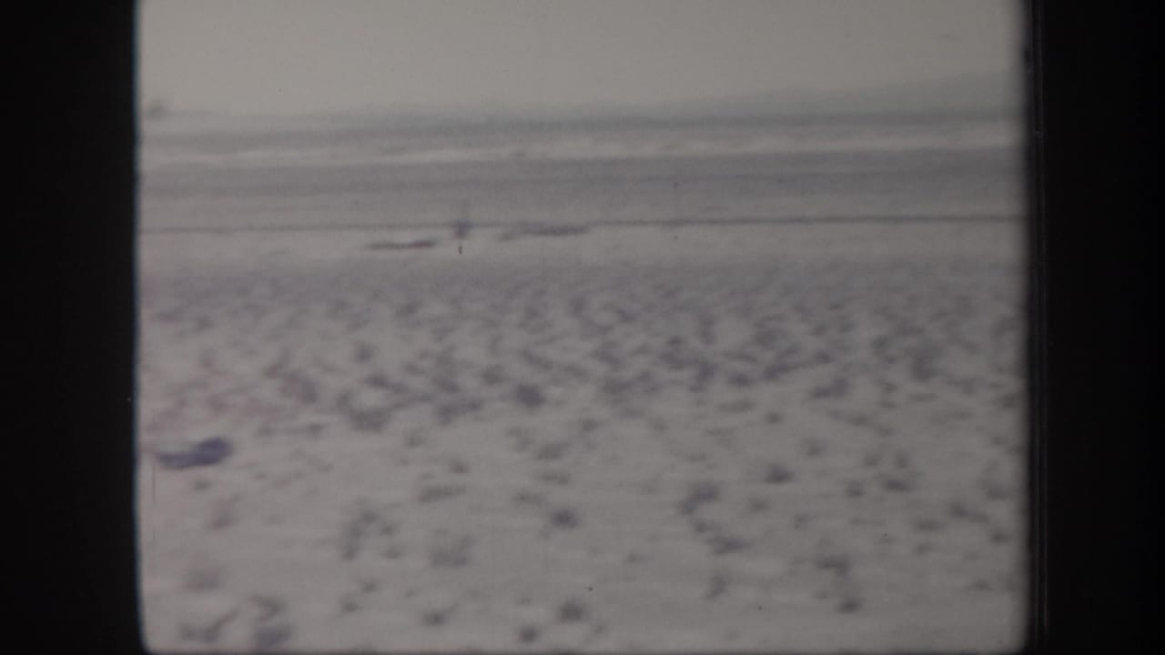 1957 Arizona 8mm home-movie frame showing an arid plain with scattered scrub, a hazy horizon, and distant low hills.