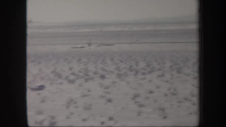 1957 Arizona 8mm home-movie frame showing an arid plain with scattered scrub, a hazy horizon, and distant low hills.