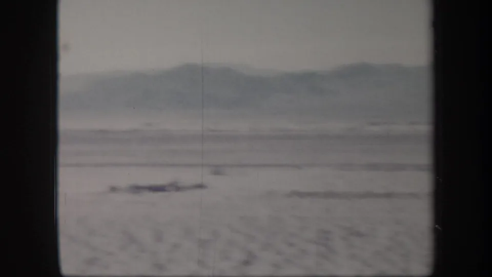 1957 Arizona desert view on 8mm film, with hazy hills beyond a flat arid plain and a small indistinct object in the distance.