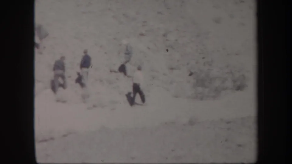 1957 Arizona home-movie frame showing several people walking across a wide arid plain beneath hazy distant hills.