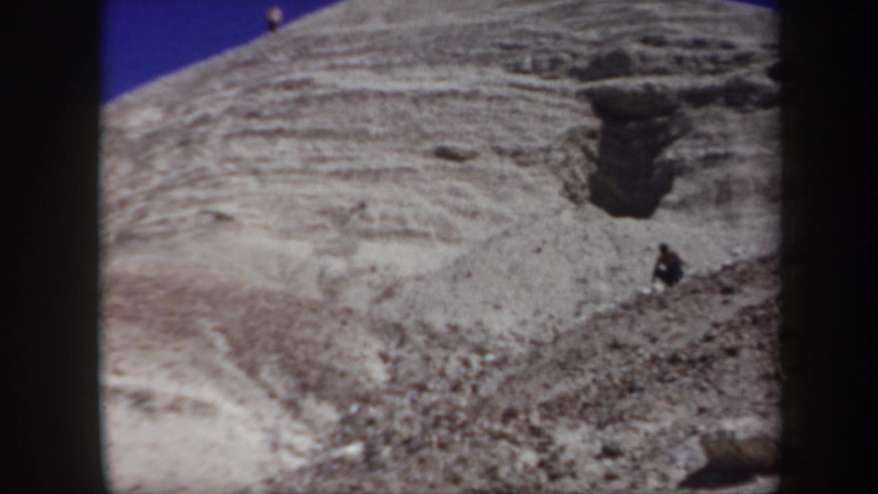 Arizona 1957 home-movie frame showing a pale rocky slope, blue sky, and a small person near the upper ridge.