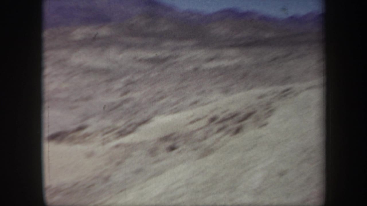 Wide view of pale desert hills and distant mountains with no clear figure visible.